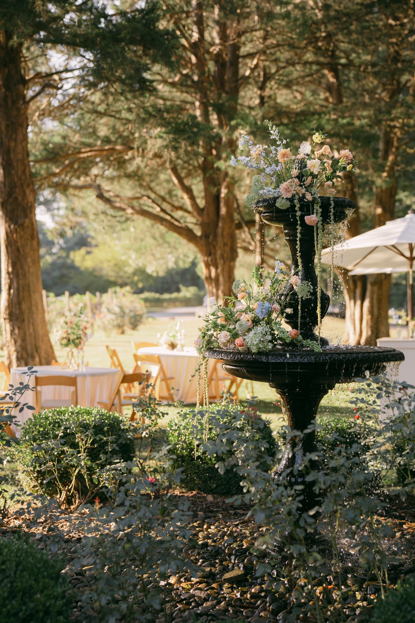 An elegant outdoor wedding reception setup featuring Noella's floral arrangements atop elevated urns, displaying a luxurious floral centerpieces and outdoor table setup.