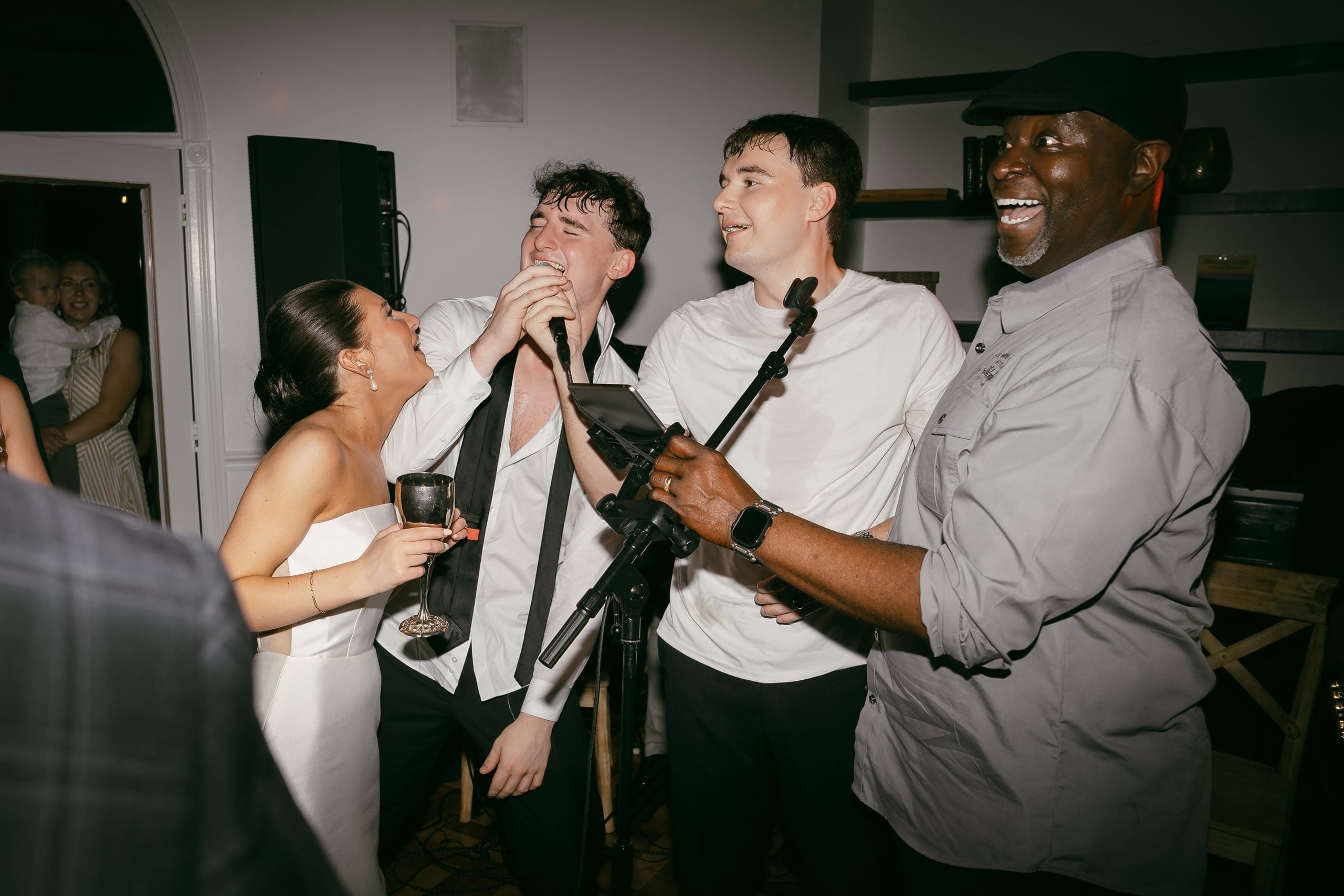 bride and groom sing into microphones with the band on a dance floor surrounded by guests, showcasing a lively reception party.