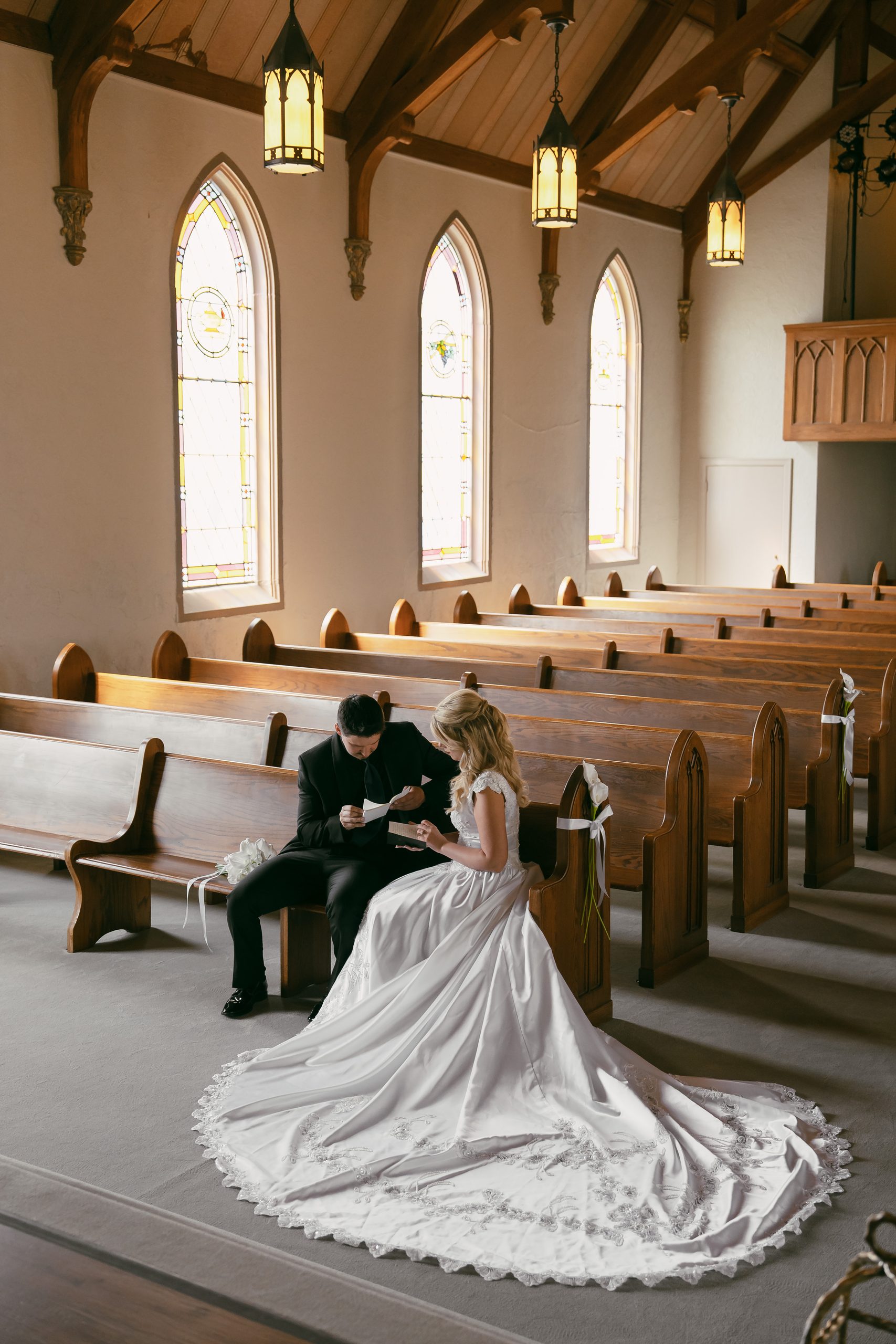 A bride in an elegant gown sits on a wooden bench inside a grand church aisle, highlighting a traditional church interior wedding location.